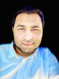 Close-up portrait of smiling young man against black background