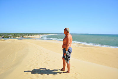 Full length of shirtless man on beach against clear sky