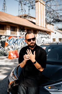 Man with beard standing against car