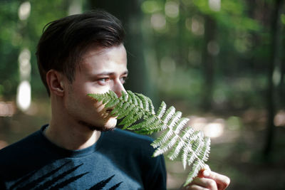 Young man looking away while holding leaves outdoors