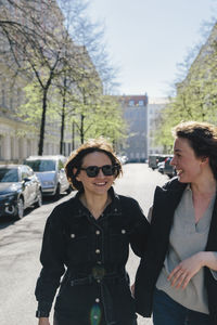 Cheerful lesbian couple walking on street in city during sunny day