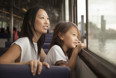 Thoughtful mother and daughter looking through window while travelling in ferry