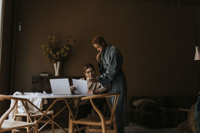 Non-binary person showing smart phone to friend doing finance at home