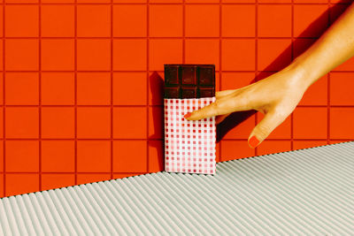 Woman hand holding dark chocolate bar against red tile wall