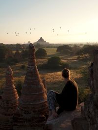 Woman sitting on landscape against sky