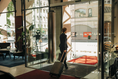 Rear view of businesswoman with suitcase leaving hotel