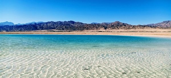 Scenic view of sea and mountains against clear blue sky