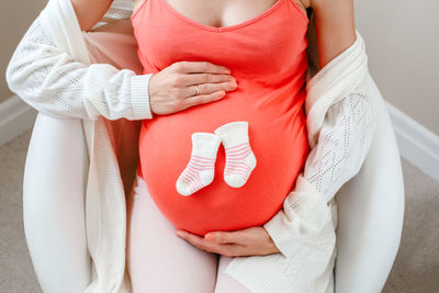 Midsection of pregnant woman sitting on chair at home