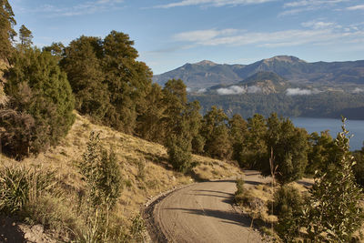 Road by trees and mountains against sky