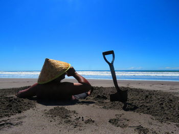Rear view of man sitting on beach against sky