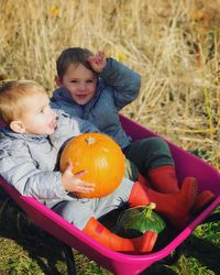 Cute siblings with pumpkin sitting in wheelbarrow at farm