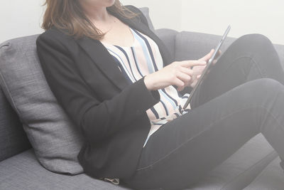 Midsection of woman using digital tablet while sitting on sofa at home