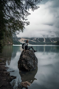 Man on rock by lake against sky
