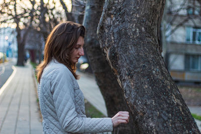 Side view of young woman against tree trunk