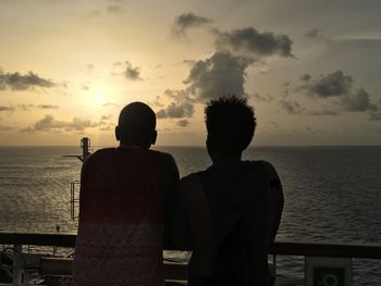 Couple looking at sea against sky during sunset