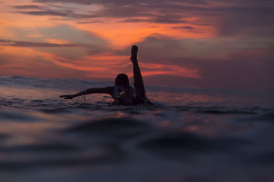 Woman swimming on surfboard in sea during sunset