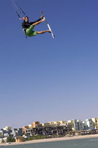 Low angle view of person jumping against clear blue sky