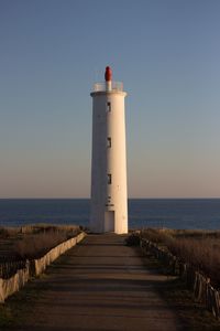 Lighthouse by sea against clear sky