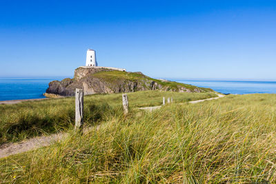 Lighthouse by sea against clear blue sky