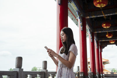 Smiling young woman using smart phone while standing at temple