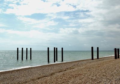 Wooden posts on beach against sky