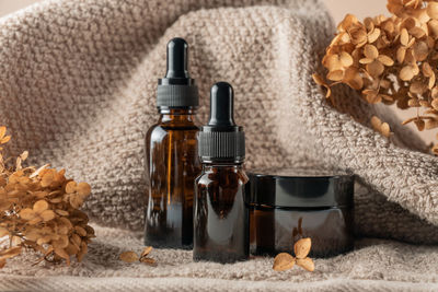 Close up of collagen cream in glass jar, serum in amber glass bottle and dry flowers on beige backg