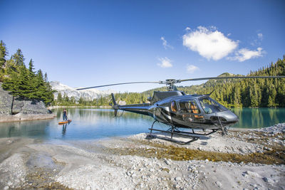 Female paddle boards on lake next to her helicopter