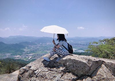 Man sitting on rock by mountain against sky