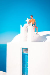 Man sitting on church against blue sky