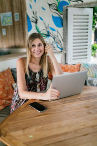 Portrait of smiling young woman using phone on table