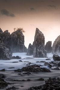 Rocks on beach against sky during sunset