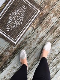 Low section of woman standing by doormat on wooden floor