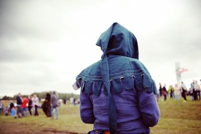 Rear view of person in hood standing on field against sky