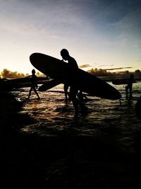 Silhouette man with surfboard on beach against sky during sunset