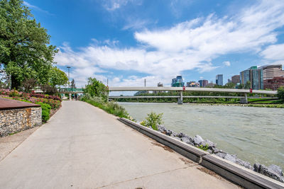 Footpath by river in city against sky