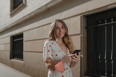 Young woman using mobile phone while standing against wall