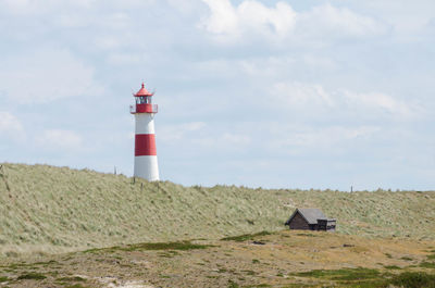 Lighthouse on field by building against sky