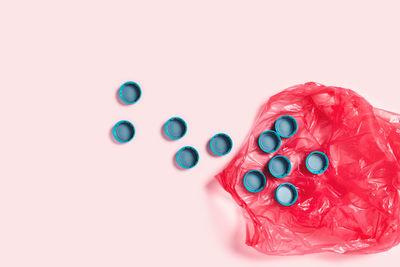 Plastic bag with surrounded by plastic bottle cups on pink background. 