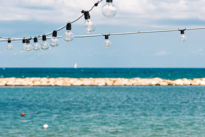 Vintage hanging light bulbs with blue sky, white clouds, blue sea, sail boat and breakwater