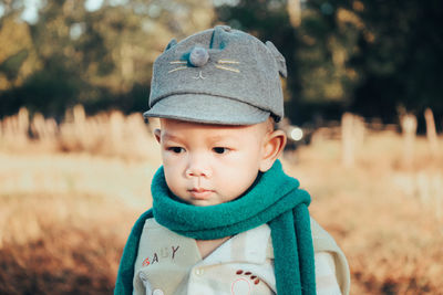 Cute baby boy wearing warm clothing and cap on land