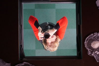 Portrait of young woman photographing through window