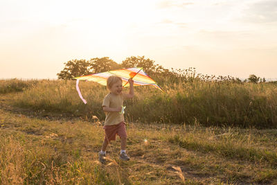 Happy little kid boy having fun with kite in nature at sunset