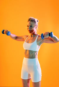Full length of woman with arms raised standing against yellow background