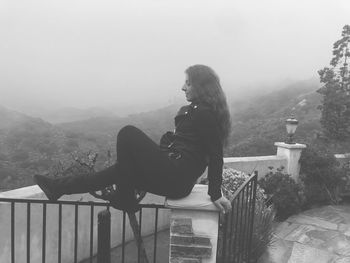 Side view of woman sitting on railing against mountain