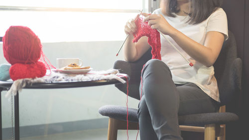 Midsection of woman knitting while sitting on chair at home