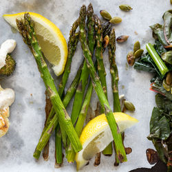Close up of roasted asparagus spears with lemon wedges.