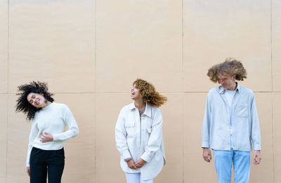 Group of young diverse women and man with curly hair standing in row against beige wall having fun
