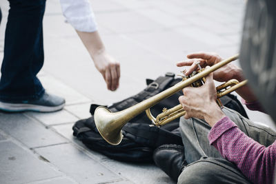 Low section of man giving money to street musician playing trumpet at footpath in city