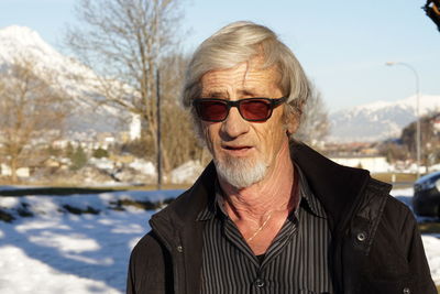 Portrait of senior man wearing sunglasses standing on snow covered road 