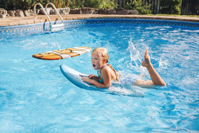 Full length of cute girl lying on paddleboard in swimming pool